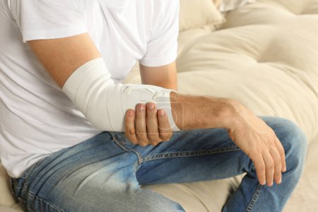Foto de Hombre con el brazo envuelto en vendaje médico en el sofá, primer plano - Imagen libre de derechos