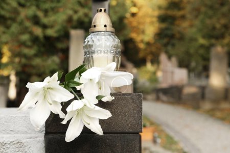 Weiße Lilien und Grablicht auf grauem Granitgrabstein im Freien, Platz für Text. Trauerzeremonie