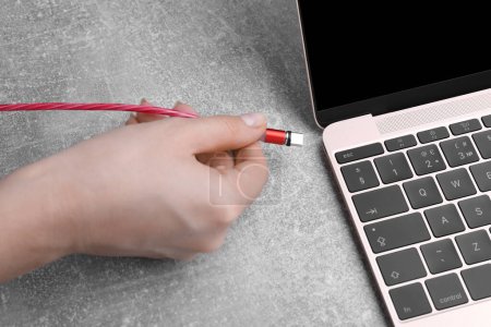 Photo for Woman plugging USB cable with type C connector into laptop port at grey table, closeup - Royalty Free Image