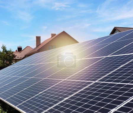 Solar panels near houses under blue sky on sunny day. Alternative energy source
