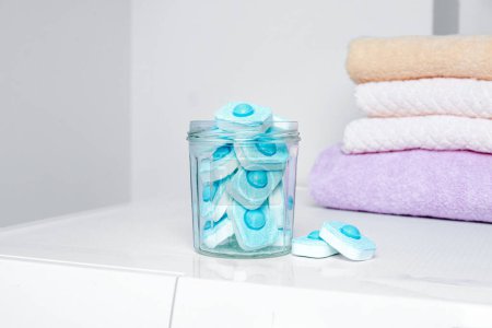 Photo for Jar with water softener tablets near stacked towels on washing machine - Royalty Free Image