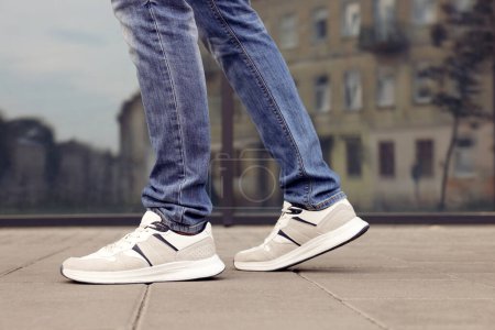 Hombre en jeans y zapatillas de deporte caminando por la calle de la ciudad, primer plano. Espacio para texto