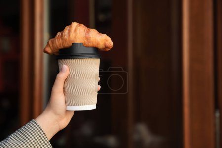 Téléchargez les photos : Femme tenant savoureux croissant et tasse de café près de la porte en bois à l'extérieur, gros plan - en image libre de droit