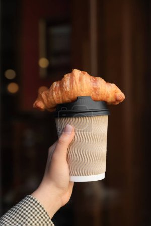 Téléchargez les photos : Femme tenant savoureux croissant et tasse de café près de la porte en bois à l'extérieur, gros plan - en image libre de droit