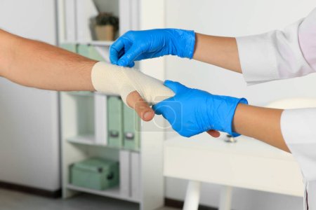 Doctor applying medical bandage onto patient's hand in hospital, closeup-stock-photo