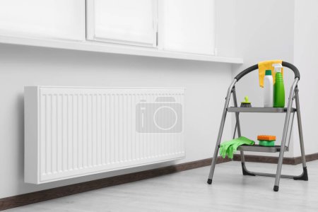 Foto de Escalera con artículos de limpieza cerca del radiador moderno en la habitación - Imagen libre de derechos