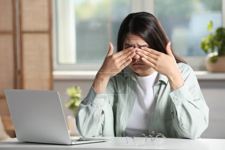 Young woman suffering from eyestrain at desk in office
