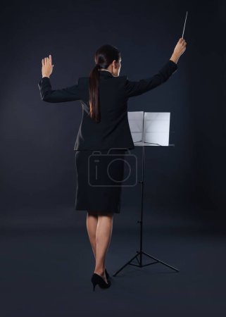 Foto de Conductor profesional con bastón y soporte de nota sobre fondo oscuro, vista trasera - Imagen libre de derechos