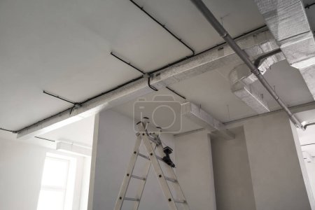Photo for Conduits with cables and ventilation system on white ceiling, low angle view. Installation of electrical wiring - Royalty Free Image