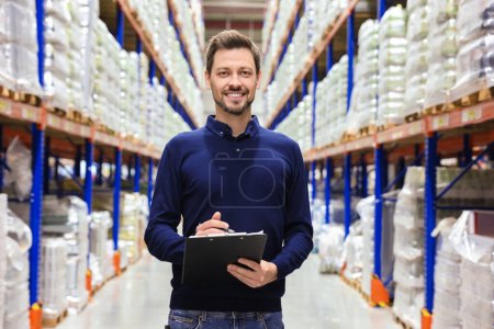 Photo for Happy manager holding clipboard in warehouse with lots of products - Royalty Free Image