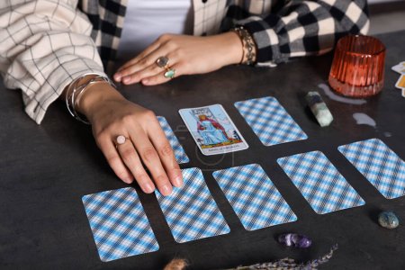 Fortune teller predicting future on spread of tarot cards at grey table, closeup