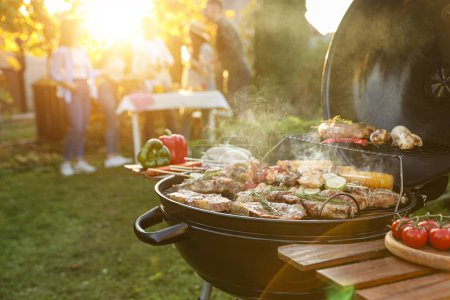 Photo for Group of friends having party outdoors. Focus on barbecue grill with food. Space for text - Royalty Free Image
