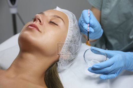 Kosmetikerin appliziert chemisches Peelingprodukt im Salon auf das Gesicht der Kundin