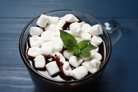 Photo for Glass cup of delicious hot chocolate with marshmallows and fresh mint on blue wooden table, closeup - Royalty Free Image