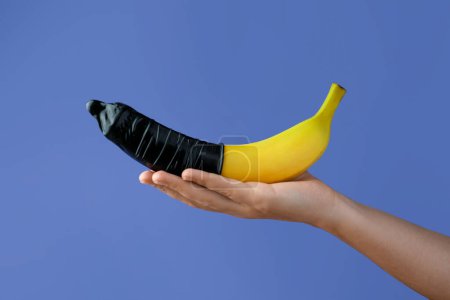Téléchargez les photos : Femme tenant une banane en préservatif sur fond bleu clair, gros plan. Concept de sexe sûr - en image libre de droit