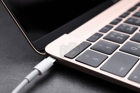 Téléchargez les photos : Câble USB avec connecteur Lightning et ordinateur portable sur table noire, gros plan - en image libre de droit