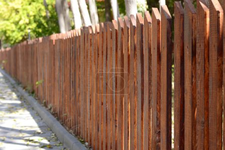 Wooden fence on sunny day near beautiful trees outdoors