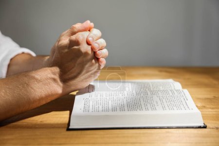 Hombre con la Biblia rezando en la mesa de madera, primer plano