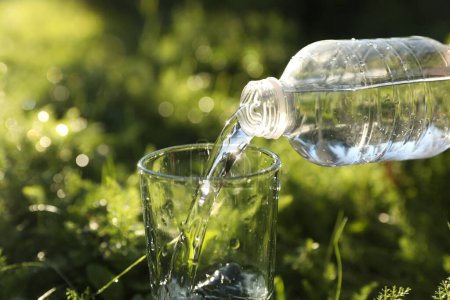 Téléchargez les photos : Verser de l'eau fraîche de la bouteille dans du verre sur de l'herbe verte à l'extérieur, gros plan - en image libre de droit