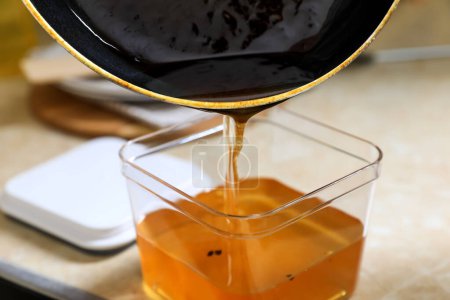 Verter el aceite de cocina usado de la sartén en un recipiente sobre una mesa beige, de cerca
