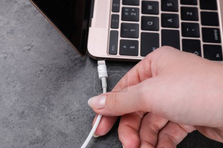 Téléchargez les photos : Femme branchant le câble USB avec le connecteur de foudre dans le port d'ordinateur portable sur la table sombre, gros plan - en image libre de droit