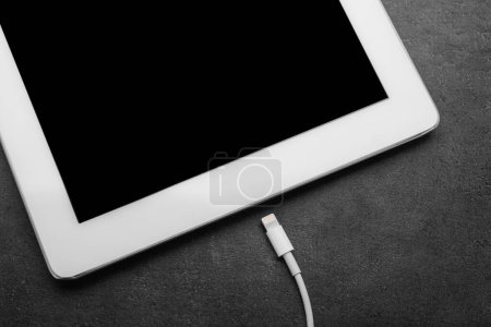Téléchargez les photos : Câble USB avec connecteur Lightning et tablette sur table noire, gros plan - en image libre de droit