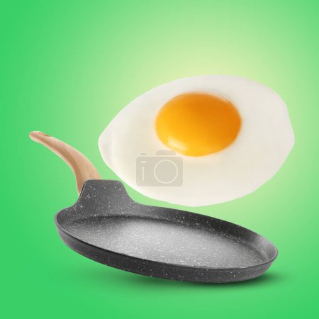 Tasty fried chicken egg falling into frying pan on color background