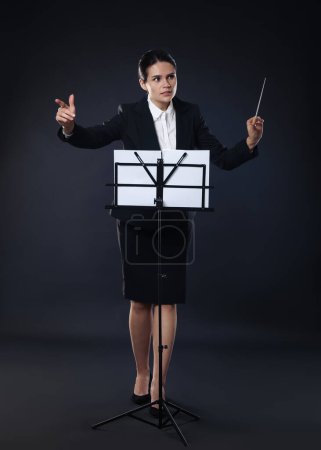 Foto de Conductor profesional con bastón y soporte de notas sobre fondo oscuro - Imagen libre de derechos