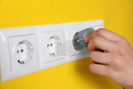 Photo for Woman inserting plug into power socket on yellow wall, closeup. Electrical supply - Royalty Free Image