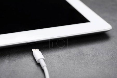 Téléchargez les photos : Câble USB avec connecteur Lightning et tablette sur table noire, gros plan - en image libre de droit