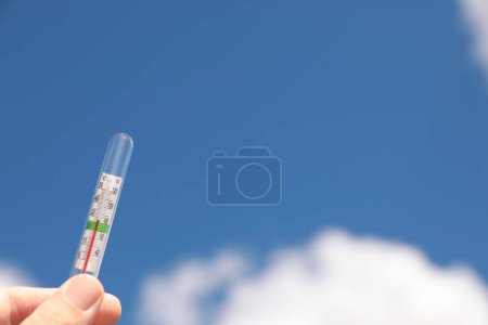 Photo for Woman holding weather thermometer against blue sky, closeup. Space for text - Royalty Free Image
