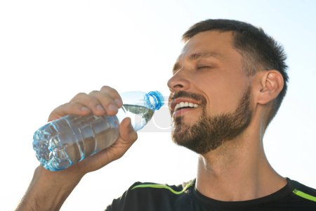 Hombre feliz bebiendo agua en el caluroso día de verano. Bebida refrescante