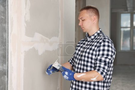 Foto de Trabajador con cuchillos de masilla y yeso cerca de la pared interior. Renovación del hogar - Imagen libre de derechos