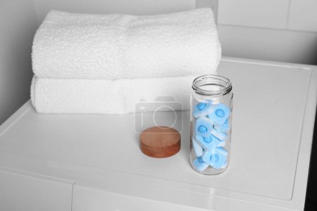 Glass jar with water softener tablets on washing machine in bathroom