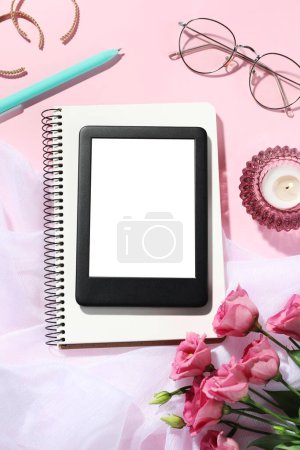 Flat lay composition with e-book reader, notebook and glasses on pink background. Space for text