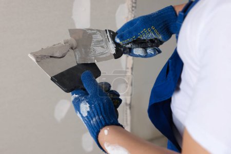 Photo for Worker with putty knives and plaster near wall indoors, closeup. Home renovation - Royalty Free Image