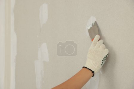 Worker plastering wall with putty knife, closeup. Space for text