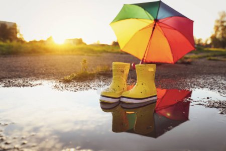 Botas de goma amarillas y paraguas en charco al aire libre, espacio para texto. Caminata de otoño