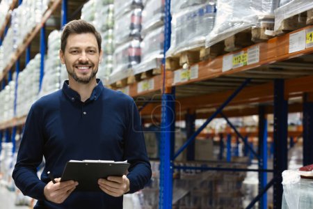 Photo for Happy manager holding clipboard in warehouse with lots of products. Space for text - Royalty Free Image