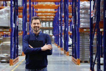 Photo for Happy manager holding clipboard in warehouse with lots of products. Space for text - Royalty Free Image
