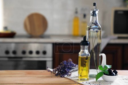Photo for Different cooking oils, olives, basil and lavender flowers on wooden table in kitchen, space for text - Royalty Free Image