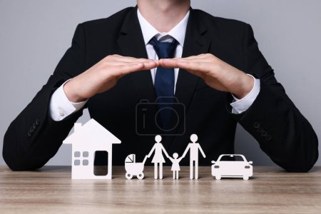 Foto de Hombre protegiendo figuras de familia, coche y casa en mesa de madera. Primer plano. Concepto de seguro - Imagen libre de derechos