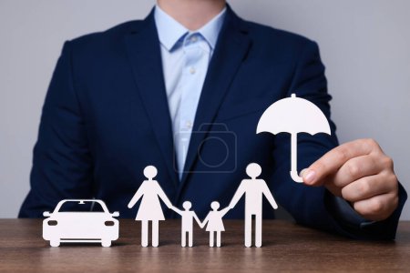Foto de Hombre sosteniendo la figura de paraguas cerca de la familia y el coche en la mesa de madera. Primer plano. Concepto de seguro - Imagen libre de derechos