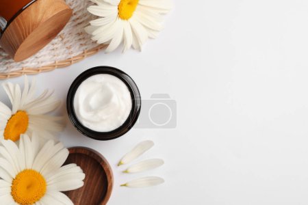 Flat lay composition with jar of face cream and beautiful flowers on white background. Space for text