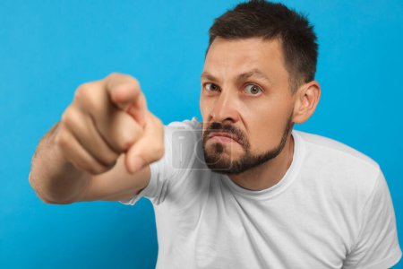 Photo for Aggressive man pointing on light blue background - Royalty Free Image