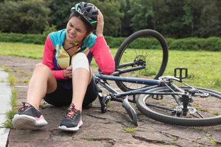 Photo for Young woman with injured knee near bicycle outdoors - Royalty Free Image