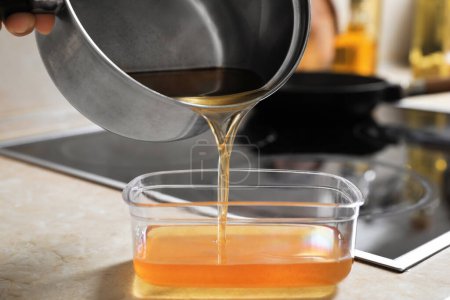 Photo for Woman pouring used cooking oil from saucepan into container on kitchen counter, closeup - Royalty Free Image
