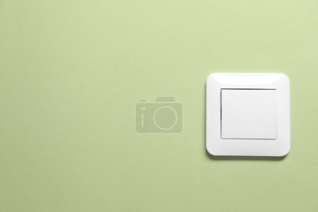 Modern plastic light switch on green background. Space for text