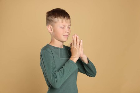 Téléchargez les photos : Garçon avec les mains jointes priant sur fond beige - en image libre de droit