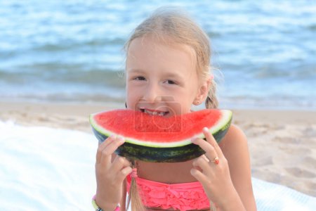 Cute little girl eating juicy watermelon on beach